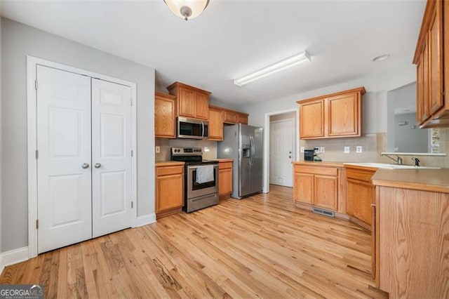 kitchen with decorative backsplash, light countertops, light wood-style floors, and appliances with stainless steel finishes