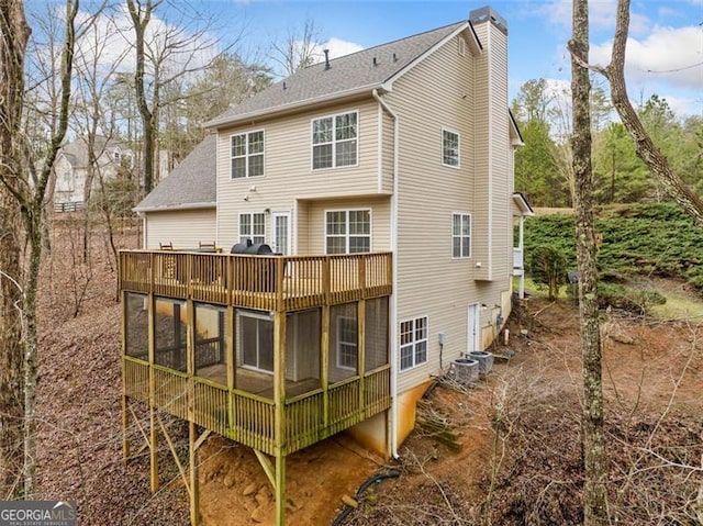 back of house with a wooden deck, roof with shingles, cooling unit, a chimney, and a sunroom