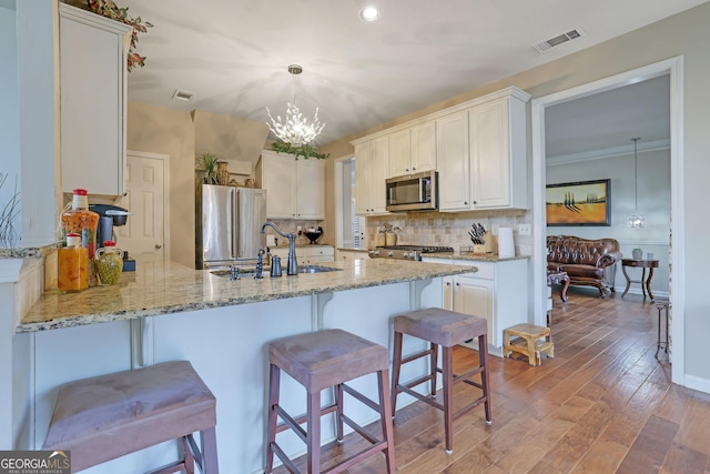 kitchen featuring visible vents, light wood-style flooring, stainless steel appliances, a peninsula, and decorative backsplash