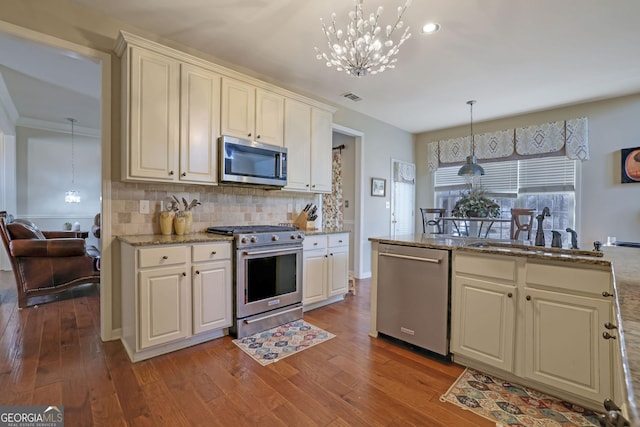 kitchen with a sink, backsplash, wood finished floors, stainless steel appliances, and light stone countertops