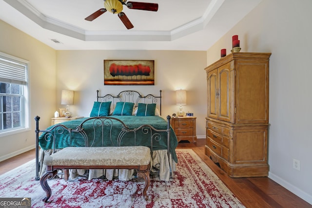 bedroom with visible vents, crown molding, baseboards, wood finished floors, and a raised ceiling