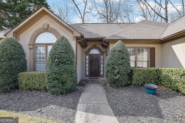 property entrance featuring stucco siding and a shingled roof