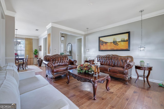 living area with visible vents, a notable chandelier, wood-type flooring, crown molding, and baseboards