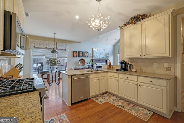 kitchen featuring light wood finished floors, a peninsula, a sink, appliances with stainless steel finishes, and a chandelier