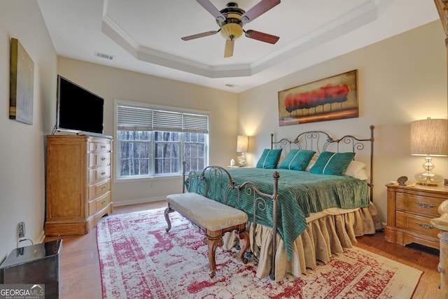 bedroom featuring visible vents, ceiling fan, ornamental molding, wood finished floors, and a raised ceiling