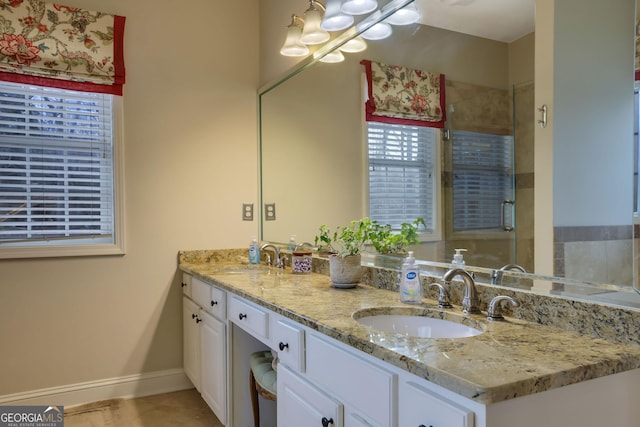 full bathroom with double vanity, a shower stall, baseboards, and a sink