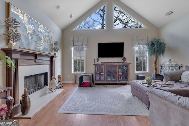 living area with high vaulted ceiling, wood finished floors, visible vents, and a fireplace with raised hearth