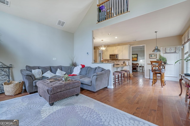 living room with visible vents, high vaulted ceiling, baseboards, and wood finished floors