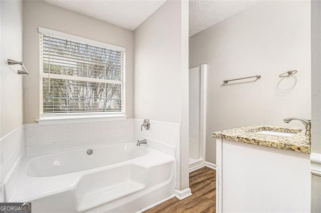 full bathroom featuring vanity, a garden tub, wood finished floors, and a textured ceiling