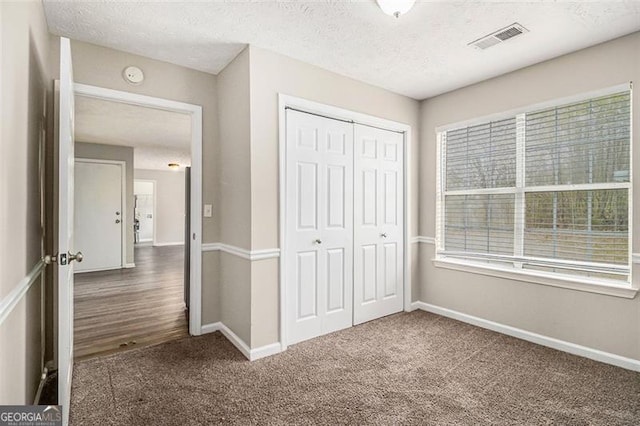 unfurnished bedroom featuring baseboards, visible vents, carpet floors, a closet, and a textured ceiling