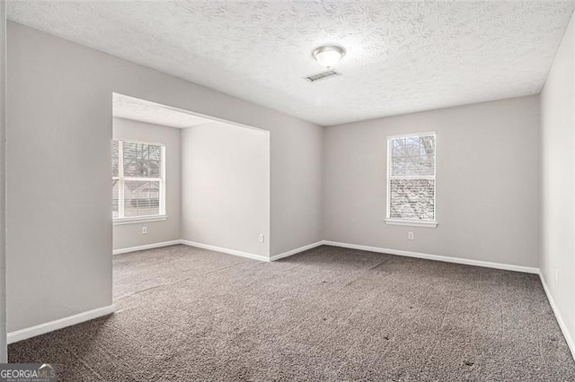 carpeted spare room featuring baseboards, visible vents, and a textured ceiling