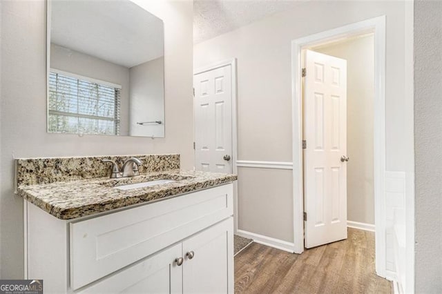 bathroom featuring a textured ceiling, vanity, baseboards, and wood finished floors