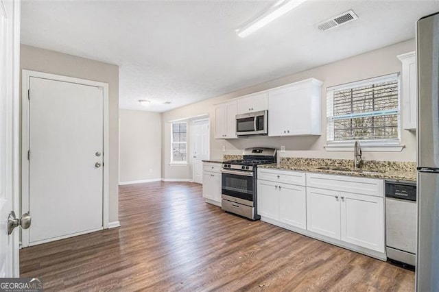 kitchen with visible vents, wood finished floors, stone countertops, stainless steel appliances, and a sink