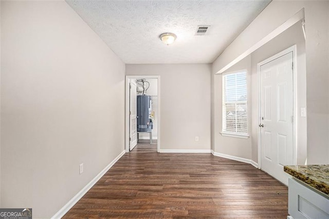 interior space with visible vents, baseboards, gas water heater, a textured ceiling, and dark wood-style flooring