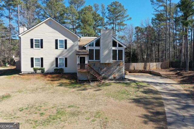 view of front of property featuring stone siding, a front yard, a chimney, and fence