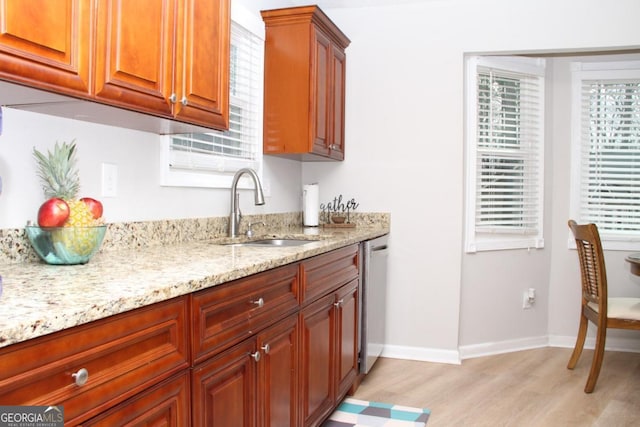 kitchen featuring a sink, baseboards, light stone countertops, light wood-type flooring, and stainless steel dishwasher