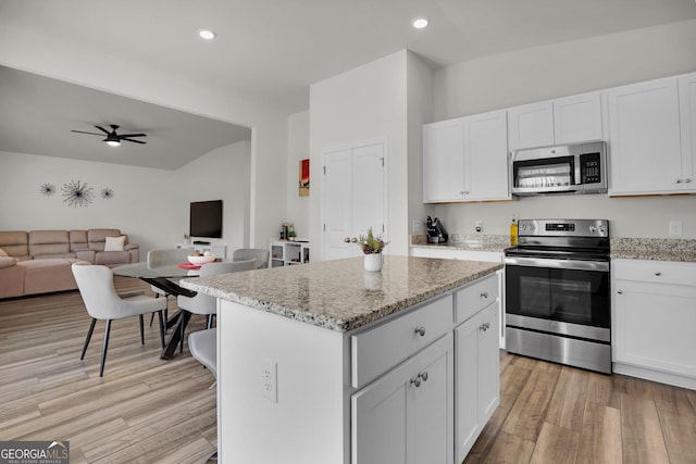 kitchen with light wood finished floors, a kitchen island, stainless steel appliances, white cabinets, and open floor plan