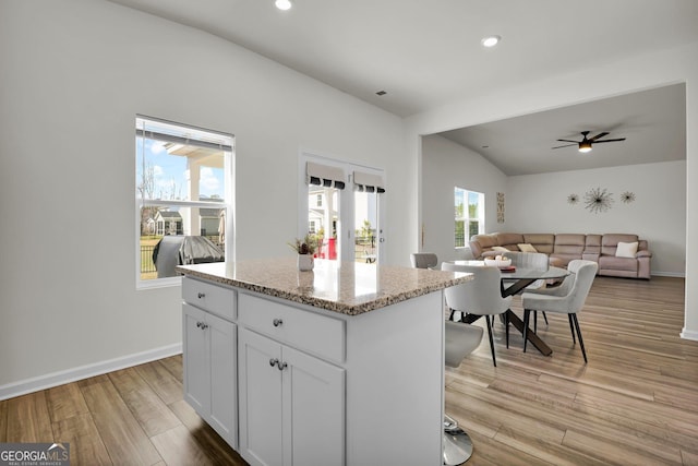 kitchen with light stone counters, baseboards, a center island, and light wood finished floors