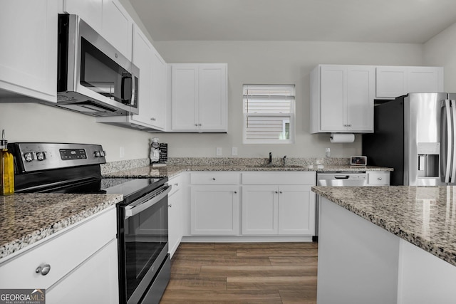 kitchen featuring wood finished floors, light stone countertops, a sink, stainless steel appliances, and white cabinetry