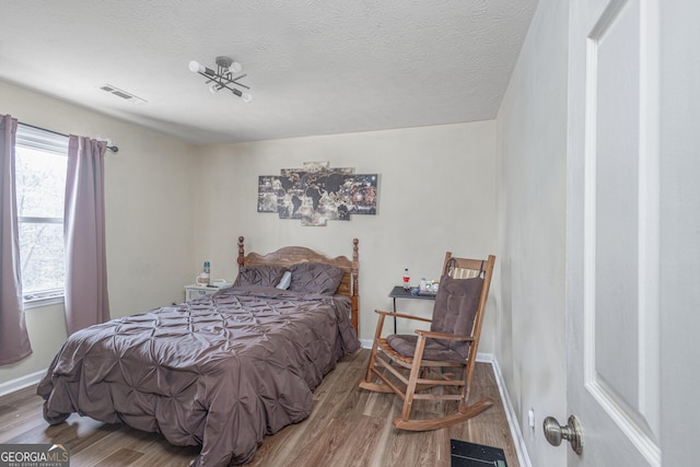 bedroom with visible vents, a textured ceiling, baseboards, and wood finished floors