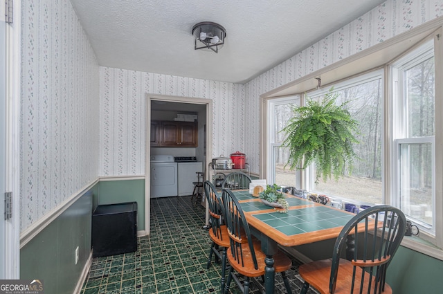 dining space with wallpapered walls, dark floors, wainscoting, a textured ceiling, and separate washer and dryer