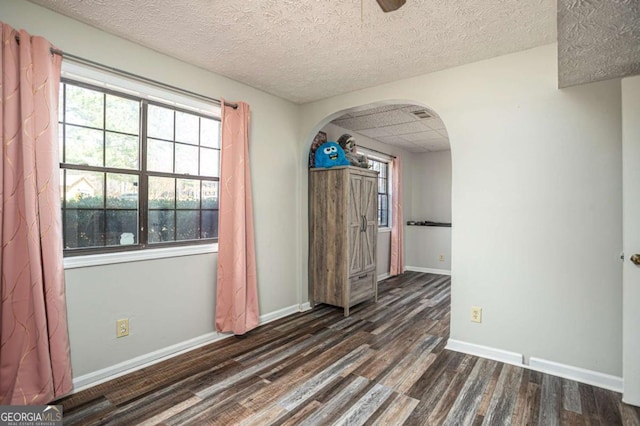 interior space featuring dark wood-type flooring, baseboards, a drop ceiling, arched walkways, and a textured ceiling