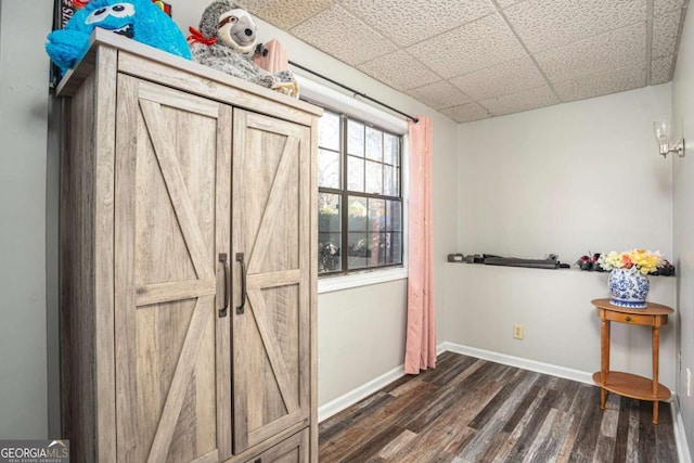 interior space featuring a paneled ceiling, baseboards, and dark wood-style flooring