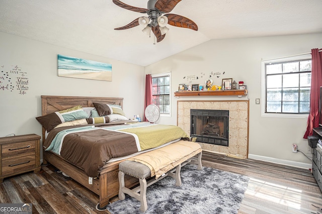 bedroom with baseboards, a tiled fireplace, vaulted ceiling, wood finished floors, and a textured ceiling