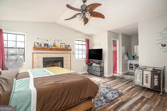 bedroom with a tiled fireplace, lofted ceiling, wood finished floors, and a textured ceiling