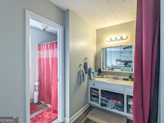 full bath featuring curtained shower, a textured ceiling, wood finished floors, baseboards, and vanity