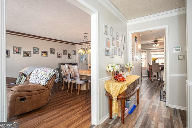 corridor featuring a wainscoted wall, a textured ceiling, wood finished floors, and crown molding