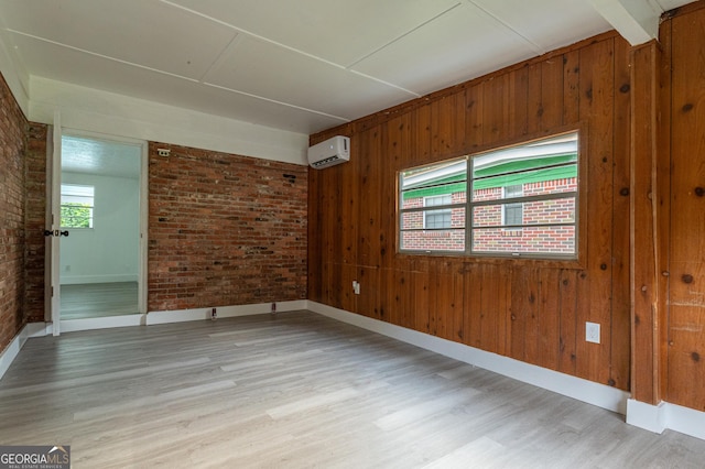 empty room featuring light wood-style flooring, brick wall, a wall mounted AC, and wood walls