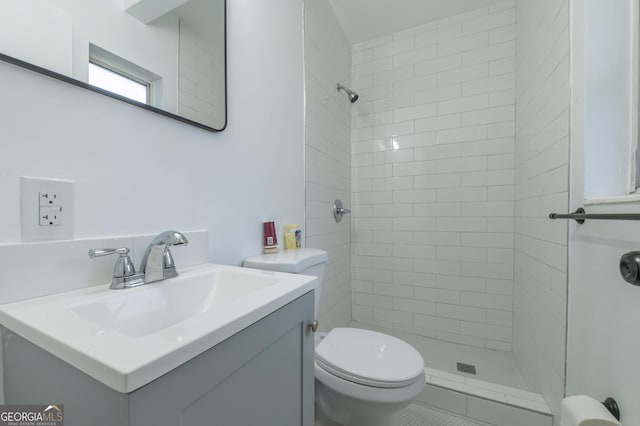 bathroom with toilet, tiled shower, and vanity