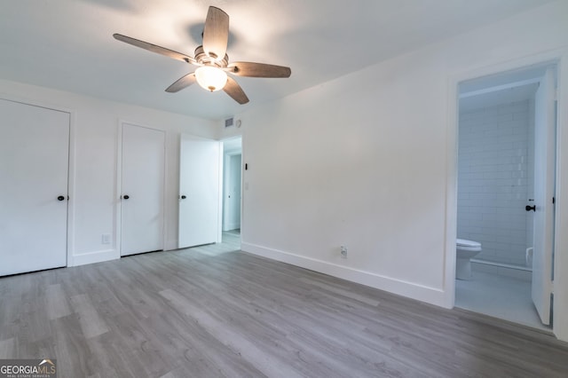 unfurnished bedroom featuring visible vents, two closets, ensuite bath, wood finished floors, and baseboards