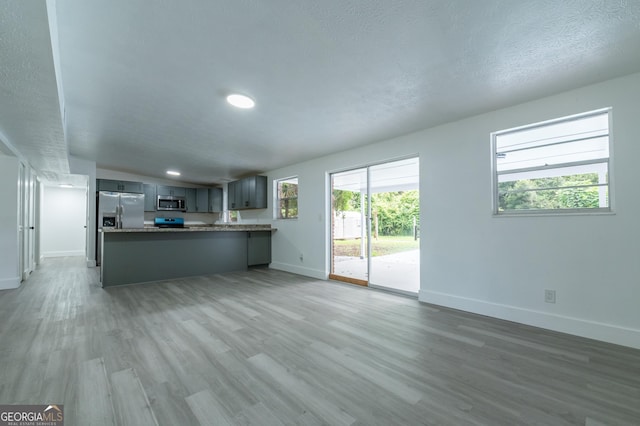 kitchen featuring baseboards, open floor plan, a peninsula, light wood-style floors, and stainless steel appliances