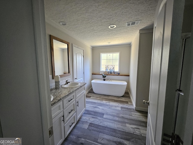 bathroom with visible vents, a freestanding bath, double vanity, wood finished floors, and a textured ceiling