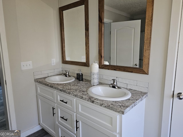 bathroom with a textured ceiling, double vanity, baseboards, and a sink