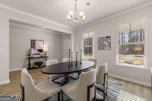 dining area featuring baseboards, visible vents, light wood-style flooring, crown molding, and a chandelier