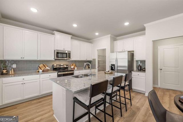 kitchen with a kitchen bar, light wood-style flooring, a sink, appliances with stainless steel finishes, and white cabinets