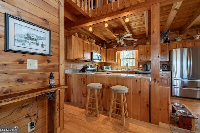 kitchen featuring wooden walls, light wood finished floors, wood ceiling, appliances with stainless steel finishes, and beamed ceiling