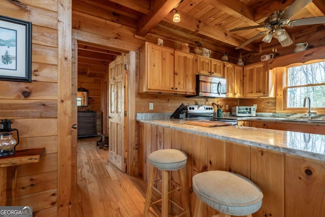 kitchen with beamed ceiling, a sink, stainless steel appliances, wooden walls, and wood ceiling