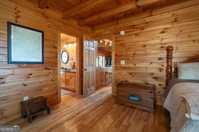 bedroom with beamed ceiling, connected bathroom, wooden ceiling, wood walls, and light wood finished floors