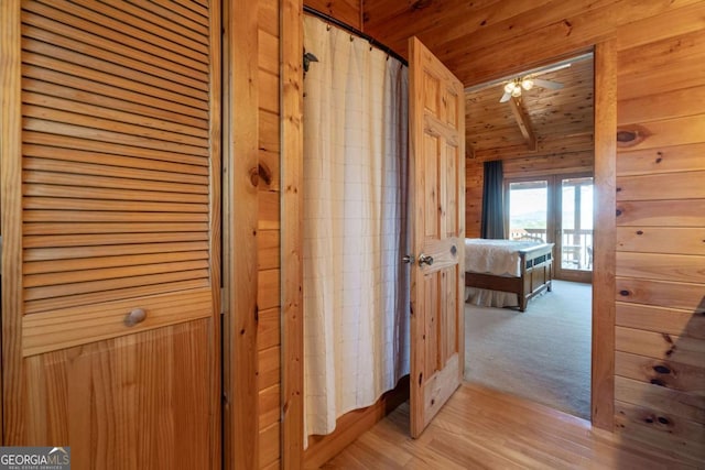 hallway featuring wooden ceiling, wooden walls, and light wood finished floors