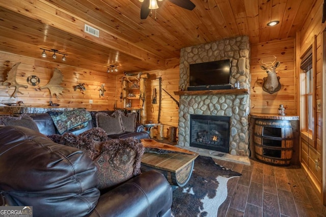 living area featuring a stone fireplace, wooden ceiling, wooden walls, and visible vents