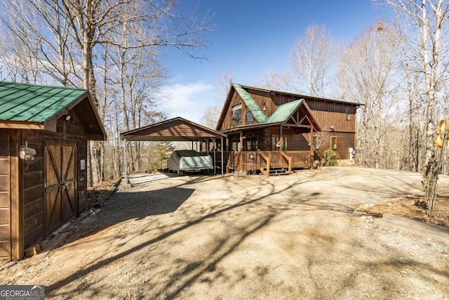 rear view of property with a carport, an outdoor structure, dirt driveway, a deck, and metal roof