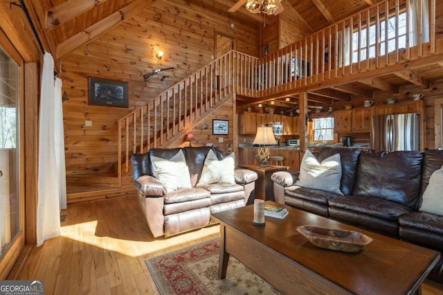 living area featuring high vaulted ceiling, stairway, wood walls, wooden ceiling, and light wood finished floors