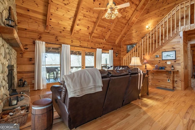 living room featuring wooden walls, a wood stove, stairs, wooden ceiling, and light wood-type flooring