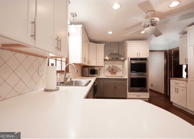 kitchen featuring backsplash, light countertops, appliances with stainless steel finishes, wall chimney exhaust hood, and a sink