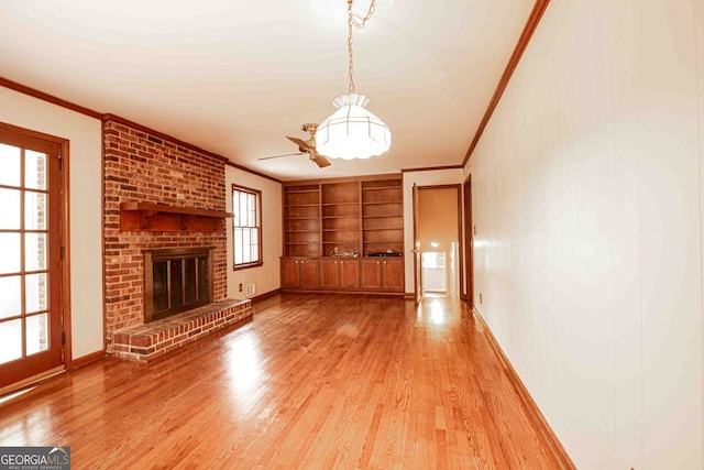 unfurnished living room featuring a brick fireplace, baseboards, built in features, light wood-type flooring, and ornamental molding