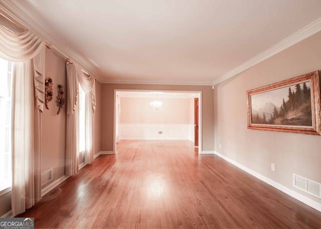 spare room with a notable chandelier, visible vents, ornamental molding, and wood finished floors